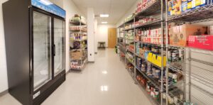 Picture of the food pantry in RAC 235. Image shows a refrigerator and shelves stocked with non-perishable food items.